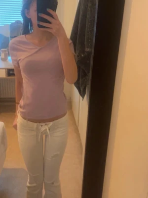 Ljuslila omlottopp med kort ärm - Säljer en ljuslila topp med omlottdetalj och korta ärmar. Toppen är i storlek 158-164 men passar även Xs för en figurnära passform och tröjan är även perfekt för dig som gillar en enkel men ändå trendig stil. Materialet känns mjukt och stretchigt, vilket gör den bekväm att bära hela dagen. Toppen är även typ aldrig använd och därför i bra skick.