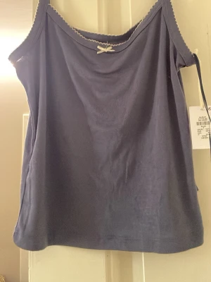 Mörkblått linne från Primark - Mörkblått loungewear-linne från Primark med tunna axelband och liten rosett framtill. Dekorativ vågig kant längs urringningen. Perfekt för chill dagar hemma. Mjukt och bekvämt material. Köptes nyligen i Berlin men ångrade mig så jag säljer den här ist💕