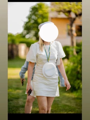 Vit kort studentklänning med puffärm - Säljer min student  klänning med puffärmar och rundad hals. Klänningen har en figurnära passform och är tillverkad i ett lätt tyg, perfekt för student eller sommar.  Den har lite öppning vid ryggen. Klassisk och stilren design utan mönster eller extra detaljer. Endast använd 1 gång å inte täcken på användning 