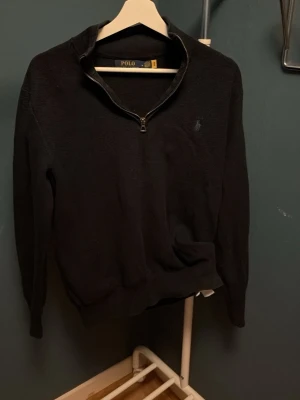 Marinblå halvzip tröja från Polo Ralph Lauren - Klassisk marinblå tröja med halv dragkedja från Polo Ralph Lauren. Tröjan har en diskret logga på bröstet och ribbade muddar vid ärmar och nederkant. Perfekt till jeans eller chinos för en clean look.