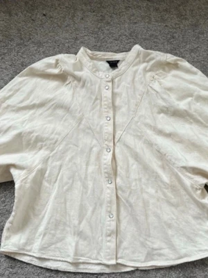 Krämvit blus med tryckknappar Lindex - Stilren krämvit blus från Lindex med rund halsringning och tryckknappar framtill. Blusen har en avslappnad passform och är tillverkad i ett mjukt tyg med diskret struktur. Perfekt att matcha med jeans eller kjol för en enkel men snygg look.