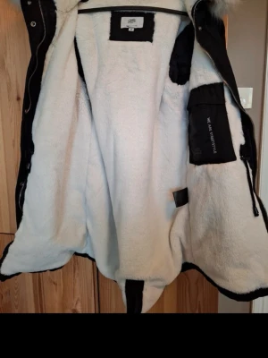 Svart parkas med fuskpäls från sixth june - Säljer en svart parkas från sixth june  med stor huva och vit päls. Jackan har mjukt vitt foder, dragkedja och knappar framtill samt flera fickor. Perfekt för kalla dagar och riktigt snygg streetstil. Orginal pris är 1999 men säljer för 1000