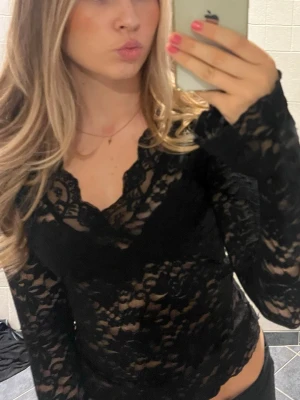 Svart spetsblus med v-ringning - Säljer en svart långärmad blus i spets med v-ringad hals. Toppen är genombruten och har en feminin, elegant look som passar perfekt till jeans eller kjol. Materialet är mjukt och följsamt, och modellen är figurnära för en snygg siluett.