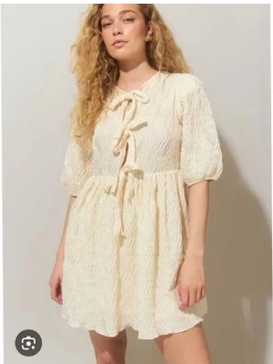 Sommarklänning❤️ - Supersöt kort klänning i ljus färg med strukturmönster och puffärmar. Klänningen har två dekorativa knyt framtill och lätt volang i kjolen. Perfekt för sommarens alla tillfällen och ger en romantisk vibe.