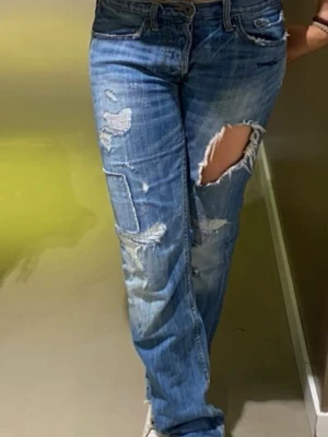 Blå Lågmidjade jeans med slitningar & hål - Säljer ett par blå jeans den american eagle med slitningar och patchade detaljer. Jeansen har en rak passform och flera revor, bland annat en stor reva på låret. Perfekta för en avslappnad och trendig look. Så så snygga!!!!! Bra skick. Waist 30 & length 34