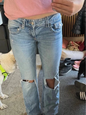 Ljusblå  jeans med hål - Säljer ett par ljusblå jeans med bootcut och stora hål vid knäna. Jeansen har klassisk femficksmodell och låg midja. Perfekta för en avslappnad och trendig look. Materialet är denim i bomull. Storlek 158