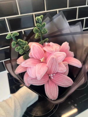 Bukett med rosa tygblommor - Säljer en fin bukett med konstgjorda blommor i rosa tyg/piprensare , formade som liljor och dekorerade med gröna blad. Blommorna är inslagna i ett mörkt, halvgenomskinligt papper. Perfekt som dekoration eller present.