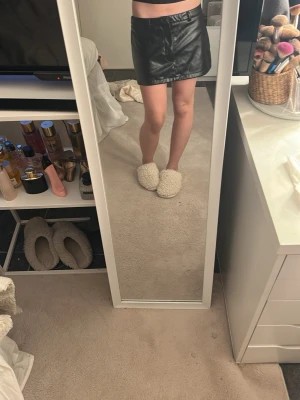 Svart kort skinnkjol - Säljer en svart kort skinnkjol med bälteshällor och enkel design. Kjolen har en rak passform och är perfekt för dig som gillar en edgy och trendig stil. Passar till många olika outfits och är ett måste i. Helt ny 