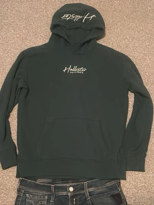 Mörkgrön Hollister Hoodie - Tvärfet hollister hoodie i oanvänt skick. Säljer för den är för stor för mig, tyvärr. Skriv vid funderingar!🔥