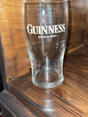 Guinness ölglas 0,4L - Säljer ett klassiskt Guinness ölglas i genomskinligt glas med vit logga och texten 'Draught' på framsidan. Glaset rymmer 0,4 liter och har en lätt rundad form som passar perfekt till öl eller andra drycker.