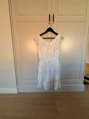 Vit spetsklänning från Lindex - Supersöt vit klänning från Lindex i storlek 36. Klänningen har flera lager volanger och är helt täckt i spets med v-ringad hals och breda axelband. Perfekt för dig som gillar romantisk och feminin stil.
