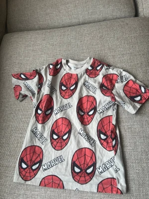 Marvel Spiderman t-shirt från H&M - Cool Marvel t-shirt från H&M med stort Spiderman-tryck över hela tröjan. T-shirten är vit med röda och svarta detaljer och har korta ärmar. Perfekt för alla Spiderman-fans som vill sticka ut med en färgglad och lekfull stil.