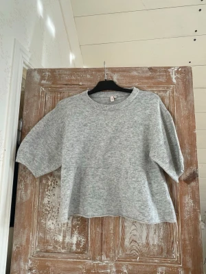 Grå oversized tröja med kort ärm - Mysig gråmelerad tröja i oversized modell med korta ärmar och rund halsringning. Perfekt för en avslappnad look och enkel att matcha med jeans eller kjol. 