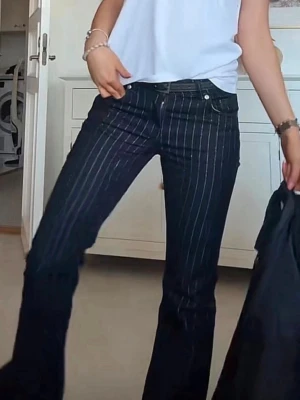Mörkblå bootcut jeans med ränder - Säljer ett par mörkblå bootcut jeans med vita vertikala ränder. Jeansen har låg midja och klassisk femficksdesign. Materialet är denim med stretch för skön passform. Perfekta för dig som gillar retrovibbar och vill sticka ut lite extra.