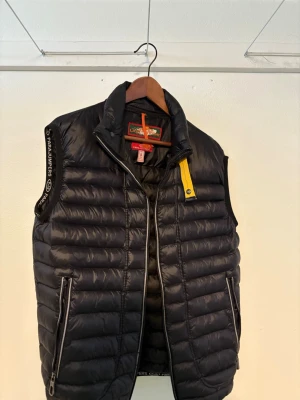 Parajumpers väst - Snygg svart dunväst från Parajumpers med gul detalj vid kragen och logga på ryggen. Västen har två dragkedjefickor fram och quiltad design. Perfekt för lager-på-lager och håller dig varm med lätt dunfyllning. Den är i gott skick ändå dåliga är att den man hänger jackan med har åkt av men annars är det inga hål i västen. Det är bara att kontakta mig vid funderingar. Det är storlek XL men är liten i storleken. 