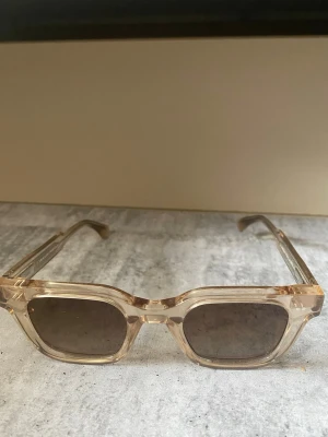 Beige fyrkantiga solglasögon - Snygga solglasögon med transparent beige båge och fyrkantig form. Glasen är mörka och ger en cool retrovibe. Perfekta för soliga dagar när du vill sticka ut lite extra.