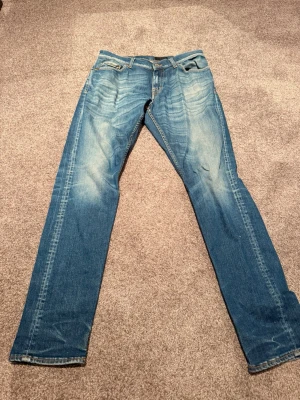 Blå slim fit jeans med slitningar - Säljer ett par blå slim fit jeans med snygga slitningar och tvättade detaljer framtill. Klassisk femficksmodell med normal midja och raka ben. Jeansen har kontrastsömmar och en läderpatch bak i midjan. Perfekta för en avslappnad och trendig look.