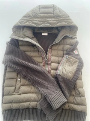 Moncler cardigan  -  Olivgrön cardigan från Moncler med huva och dragkedja framtill. Västen har ribbade muddar, ficka med dragkedja på ärmen och detaljer i stickad ull. Materialmix av nylon och ull för både värme och stil. Självklart äkta, men säljer för jag har vuxit ur den!, skriv för fler frågor !🤩🤝