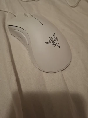 Vit gamingmus från Razer - Säljer en vit gamingmus från Razer med sladd och två sidoknappar. Musen har en stilren design med Razers logotyp på ovansidan och passar perfekt för gaming eller arbete vid datorn.