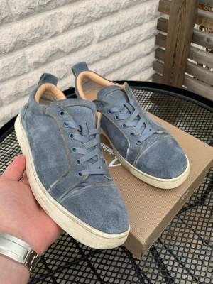 Ljusblåa sneakers från Christian Louboutin - Snygga blåa sneakers i mocka från Christian Louboutin med klassisk röd sula. Skorna har lågt skaft, matchande blå skosnören och beige innerfoder. Skorna har täcken på användning och det syns på sulan på insidan men inget som direkt märks av. Perfekta skor inför sommaren. Hör av dig vid minsta fundering och pris kan diskuteras! 💯🤩