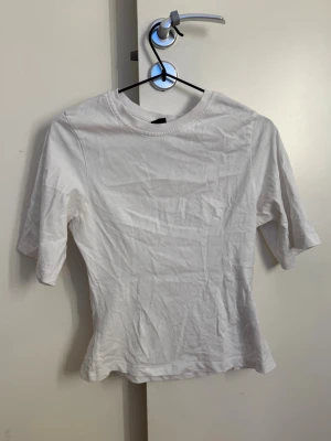 Vit  figursydd t-shirt  - En enkel vit t-shirt med rund hals och korta ärmar. Tillverkad i mjuk bomull och har en klassisk passform som funkar till det mesta. Perfekt att matcha med jeans eller kjol för en clean look.