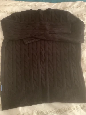 Svart kabelstickad tröja - En svart kabelstickad tröja med rund hals och långa ärmar. Tröjan har ett klassiskt flätmönster och ribbstickade muddar vid ärmslut och nederkant. Perfekt för att hålla sig varm under kyliga dagar.