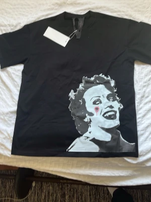 Svart Vlone t-shirt - Cool svart t-shirt med ett stort grafiskt tryck av ett ansikte i vitt och grått med röd detalj på framsidan. Baksidan har ett rött motiv med vita detaljer. Klassisk passform och rund hals. Perfekt för dig som gillar statement-plagg.