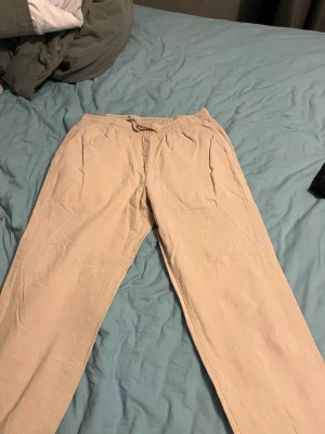 Beige linnebyxor med resårmidja - Snygga beige linnebyxor med avslappnad passform och resår i midjan samt dragsko. Byxorna har raka ben och sidofickor, perfekta för en chill och stilren look. Tillverkade i ett lätt och luftigt linnematerial.