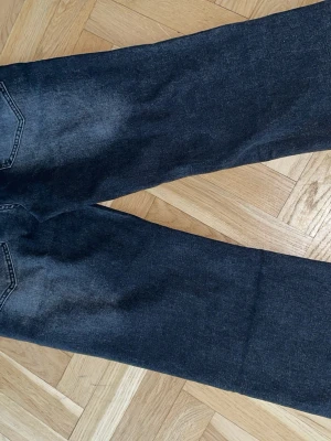 Svarta flair jeans - Säljer ett par svarta jeans med rak passform och snygg tvättad look. Jeansen har hög midja, fem fickor och rå, fransig kant längst ner på benen. Perfekta för en avslappnad och trendig stil.
