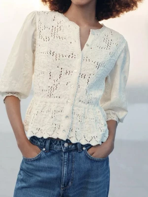 Vit spetsblus med knappar - Romantisk vit blus med spetsdetaljer och dekorativa knappar framtill. Blusen har trekvartsärm och lätt puffade axlar. Materialet är en blandning av spets och tunn bomull, vilket ger en luftig och feminin känsla. Perfekt att styla med jeans för en trendig look. SLUTSÅLD OCH EFTERTRAKTAD