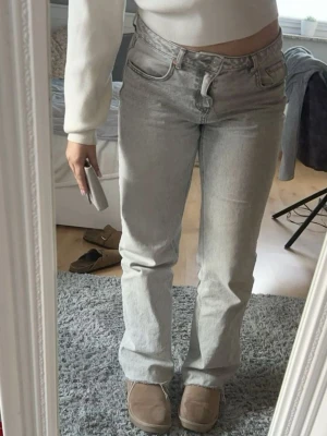 Ljusgrå raka jeans - Säljer ett par ljusgrå jeans med rak passform och hög midja. Jeansen har klassiska fem fickor och bälteshällor. Perfekta för en avslappnad och trendig look.