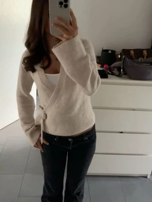 Beige omlottkofta med knytband - Mysig beige omlottkofta med knytband i sidan och långa ärmar. Koftan har en mjuk stickad känsla och en avslappnad passform, perfekt att slänga över ett linne eller t-shirt. Enkel och stilren design som passar till det mesta.