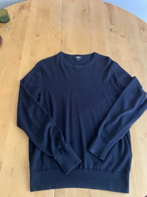Mörkblå stickad tröja från Uniqlo - En stilren mörkblå stickad tröja från Uniqlo med rund halsringning och långa ärmar. Tröjan har ribbade muddar vid ärmslut och nederkant, vilket ger en snygg passform. Perfekt för lager på lager och enkel att matcha med olika outfits.