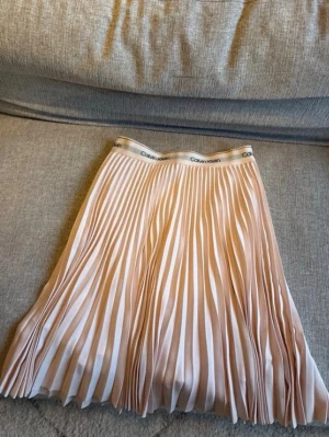 Plisserad rosa kjol från Calvin Klein - Säljer en snygg plisserad rosa kjol från Calvin Klein med elastisk midja där loggan syns tydligt. Kjolen har en luftig känsla och är perfekt för dig som gillar en stilren och trendig look.