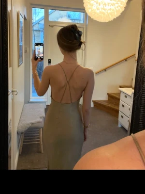 Champagnefärgad långklänning med öppen rygg - Säljer en elegant långklänning i champagnefärg med smala axelband som korsas i ryggen. Passar XS också. Klänningen har en figurnära passform och är tillverkad i ett glansigt material som ger en lyxig känsla. Perfekt för speciella tillfällen som t.ex. bal.💕
