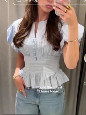 Ljusblå blus med puffärm från Zara - Supersöt ljusblå blus från Zara med puffiga korta ärmar, knappar framtill och markerad midja med volang nedtill. Helt ny med prislapp kvar✨Blusen har en feminin siluett och är tillverkad i ett lätt tyg som ger en fräsch känsla.