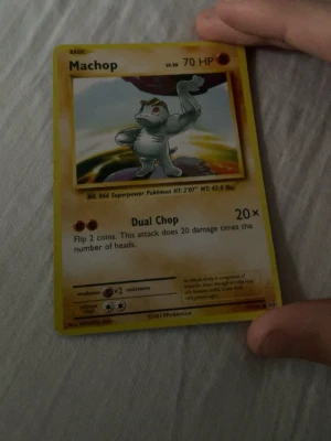 Machop Pokémonkort 2011 - Machop Pokémonkort från 2011 med gul ram och klassisk design. Kortet har 70 HP och attacken Dual Chop. Framsidan visar Machop mot en färgglad bakgrund och baksidan har den ikoniska Pokéballen. Perfekt för samlare eller Pokémonfans.