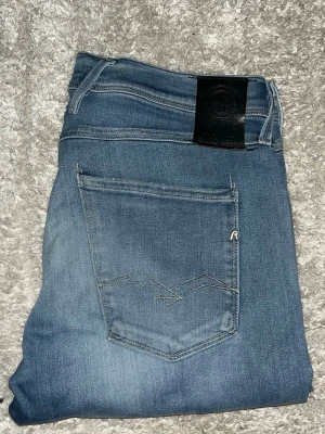 Replay Anbass jeans  - Säljer ett par blå slim jeans från Replay med klassisk femficksdesign och svarta läderpatch bak i midjan. Jeansen har diskreta slitningar och är tillverkade i stretchigt denimtyg för en bekväm passform. Perfekta för en avslappnad och trendig look. JAG SKICKAR EJ FLER BILDER PÅ JEANSEN! för storleksguide hänvisar jag till måtten och för bättre inblick i passformen rekommenderar jag att googla på modellnamnet. :) 1,106