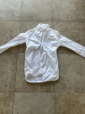 Vit klassisk skjorta med knappar - Säljer en vit skjorta med klassisk krage och knappar framtill. Skjortan har långärmad design och är tillverkad i bomull, perfekt för dig som gillar en clean och enkel look. Passar till många olika outfits och är ett måste i garderoben.