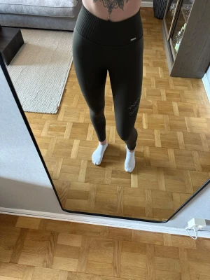 Mörkgröna träningstights från amin - Snygga mörkgröna träningstights med hög midja och mönsterdetaljer på benen. Använda endast ett fåtal gånger. Jag är 168cm