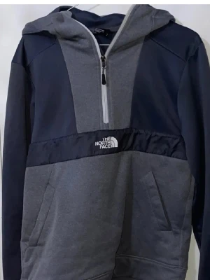 Grå och marinblå hoodie The North Face - Snygg hoodie från The North Face i grått och marinblått med halv dragkedja framtill och stor huva. Hoodien har en stor ficka på magen och logga broderad på bröstet. Tillverkad i mjukt sweatshirtmaterial, perfekt för chill eller streetwear. Tröjan är stor i storleken där det står S men passar även för storlek S
