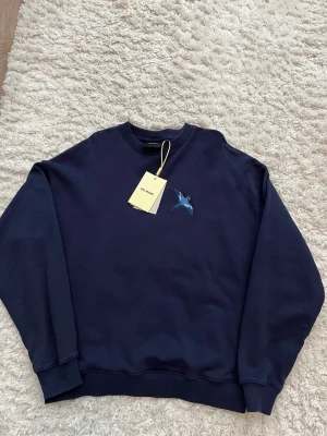 Mörkblå sweatshirt från Axel Arigato - Mörkblå sweatshirt från Axel Arigato med rund halsringning och ribbade muddar. På bröstet finns ett broderat motiv av en blå fågel. Tröjan är i mjuk bomull och har en clean, avslappnad passform. Perfekt för en stilren och modern look. Använd ca 2-3 gånger. Skick: 9/10 nypris:1850, mitt pris 1250🤩