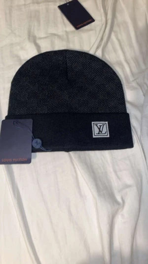 Svart mössa - Exklusiv mössa med diskret rutigt mönster och vikt kant. Snygg och stilren design som lyfter din vinterlook. Materialet känns mjukt och lyxigt, perfekt för kalla dagar. 