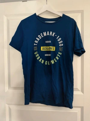 Blå Jack & Jones t-shirt med tryck - Snygg blå t-shirt från Jack & Jones med rund hals och tryck i vitt, gult och grönt framtill. Klassisk passform och korta ärmar. Perfekt för dig som gillar streetwear och vill ha en enkel men stilren look.