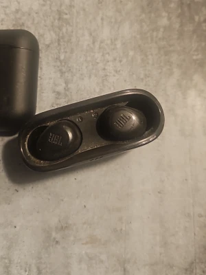JBL svarta trådlösa .... 100kr - Säljer ett par svarta trådlösa in-ear hörlurar från JBL med tillhörande laddningsetui. Hörlurarna har en stilren och kompakt design i plast, perfekt för musik 