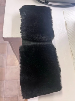 Svart fluffigt hårband - Säljer ett svart hårband med mjuk och fluffig fuskpäls. Hårbandet har en bred design och en twist framtill som ger en trendig look. Perfekt för att hålla håret på plats och addera en mysig touch till din outfit.