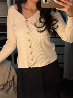 Beige ribbad kofta med knappar - Snygg beige ribbad kofta med v-ringning och långa ärmar. Koftan har en rak passform och knäpps med silvriga knappar framtill. Perfekt att slänga över ett linne eller topp för en chill look. Köp direkt för 99kr via köp nu!!😍