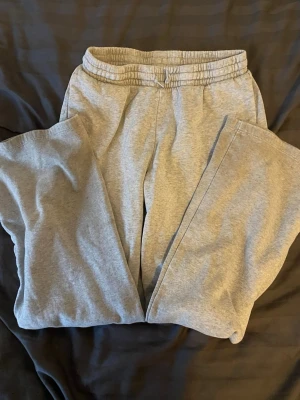 Grå mjukisbyxor från H&M - Säljer ett par grå mjukisbyxor från H&M med elastisk midja och dragsko. Byxorna är tillverkade av 80% bomull och 20% polyester, vilket gör dem riktigt sköna och mjuka. Perfekta för chill dagar eller när du vill ha något bekvämt på dig.