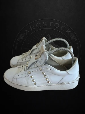 Valentino rockstud. - Säljer ett par vita sneakers från Valentino med coola silverfärgade nitar längs sidorna och bak på sulan. Skorna är i läder och har klassisk låg profil med vita snören och gummisula. Perfekta för dig som vill sticka ut med en edgy detalj.