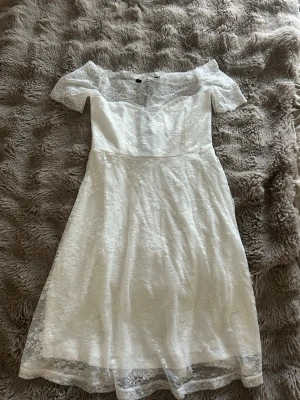 Vit spetsklänning offshoulder - Romantisk vit klänning med offshoulder och kort ärm. Klänningen är täckt av vacker spets och har en feminin, utsvängd form. Perfekt för somriga tillfällen eller studentfirande.